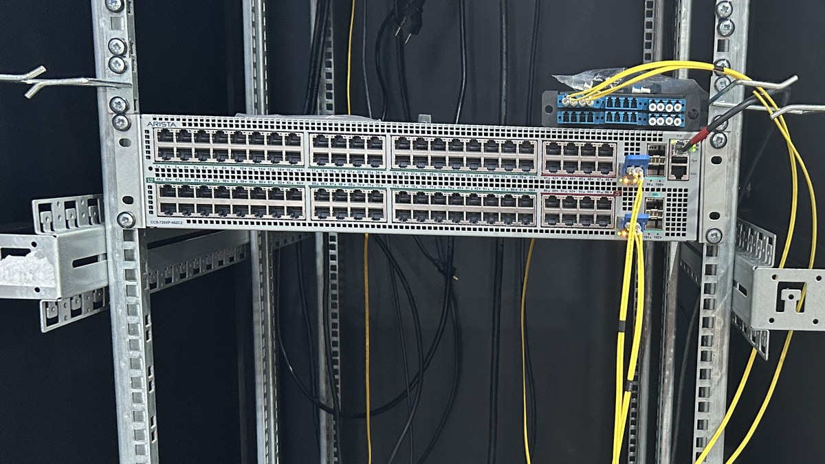 Kabine monte edilmiş, ön panelinde Arista logosu olan ağ anahtarı ve sarı fiber kablolar (temsili)