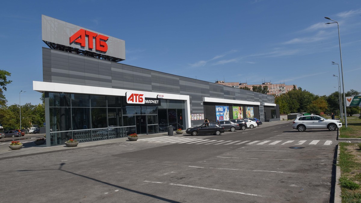 Ukrayna'da çatısında kırmızı ATB tabelası bulunan gri cepheli ATB-Market süpermarketi ve önündeki otopark