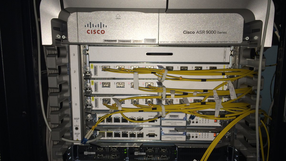 Kabinde sarı fiber kablolarla bağlı bir Cisco ASR 9000 Series yönlendirici kasası; kurumsal ağ altyapısını gösteren temsili fotoğraf (Catalyst SD-WAN bileşeni ya da etkilenen cihaz değildir)