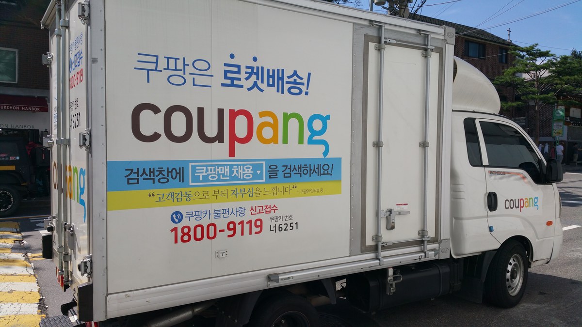 Seul'de bir sokakta Coupang logolu beyaz teslimat kamyoneti