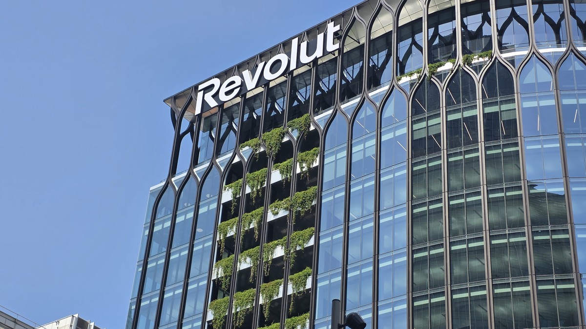 Londra'daki Revolut merkez binasının cam cephesi ve çatı katındaki beyaz Revolut logosu, mavi gökyüzü önünde