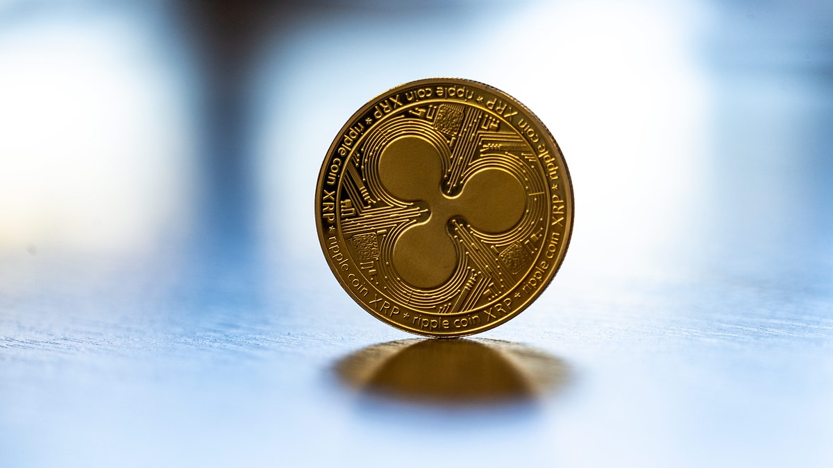 Bulanık açık mavi arka plan önünde parlak yüzeyde dik duran altın renkli madalyon; ön yüzde Ripple logosu, kenarında ripple coin XRP yazısı okunuyor (temsili fotoğraf)