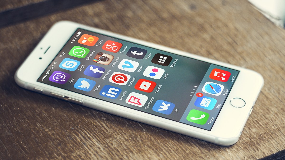 Ahşap masa üzerinde ana ekranında sosyal medya ve mesajlaşma uygulaması simgeleri görünen akıllı telefon (temsili görsel, 2017)